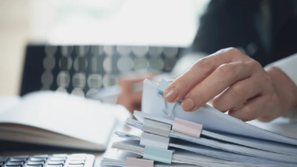 Ruka prelistava dokumente sa obeleživačima u kancelarijskom okruženju