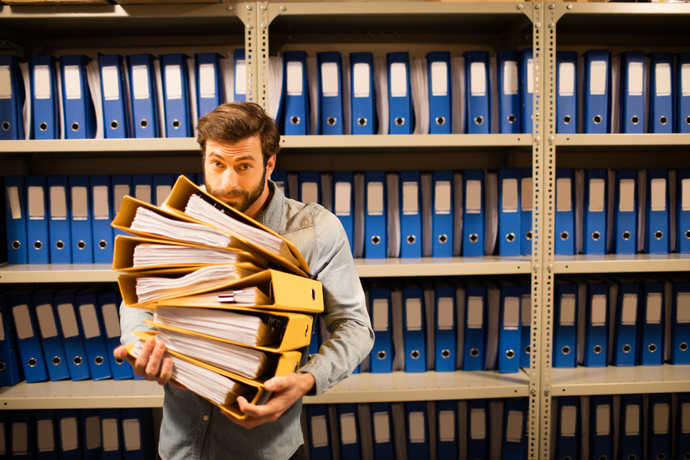 Muškarac nosi fascikle sa dokumentima ispred police pune registratora u arhivi