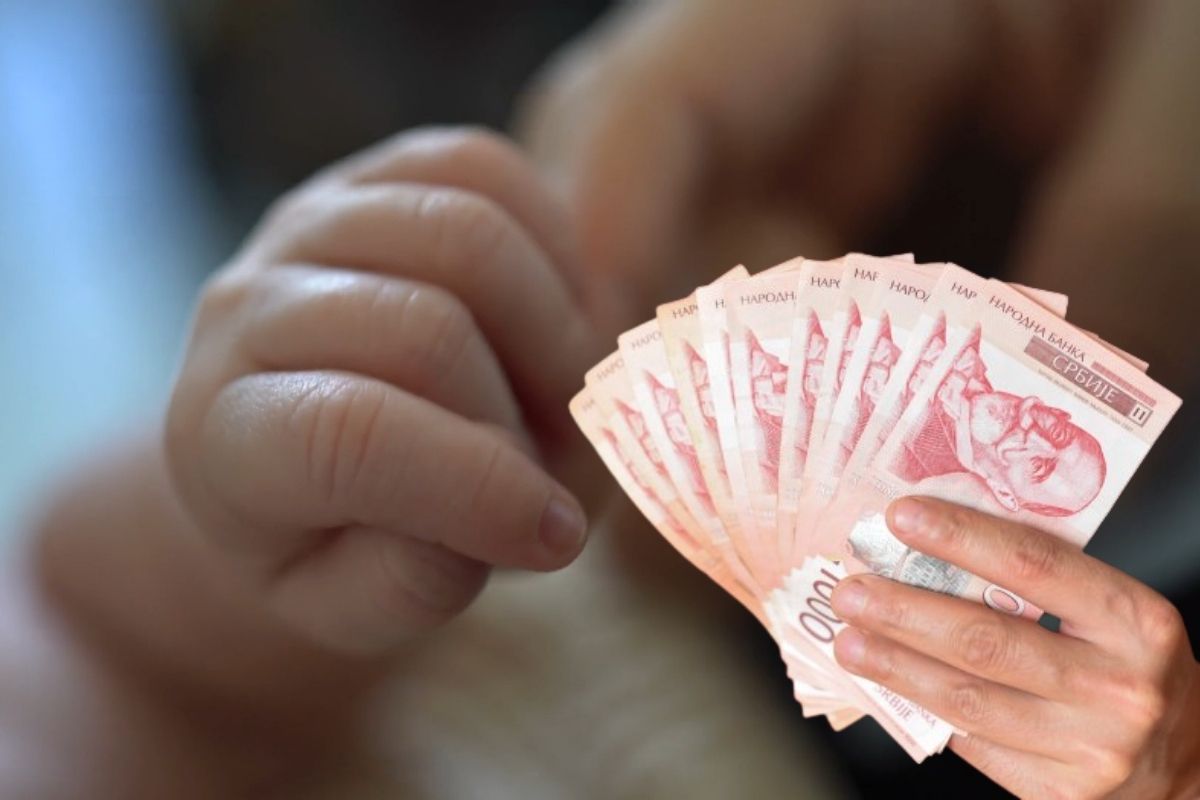 beba drži osobu za ruku, pored u ruci srpski novac