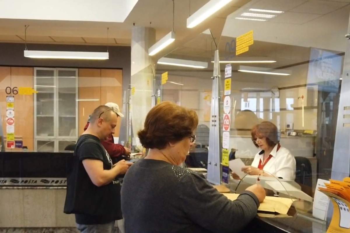 starija gospodja stoji na šalteru u pošti i podnosi prijavu za turistički vaučer